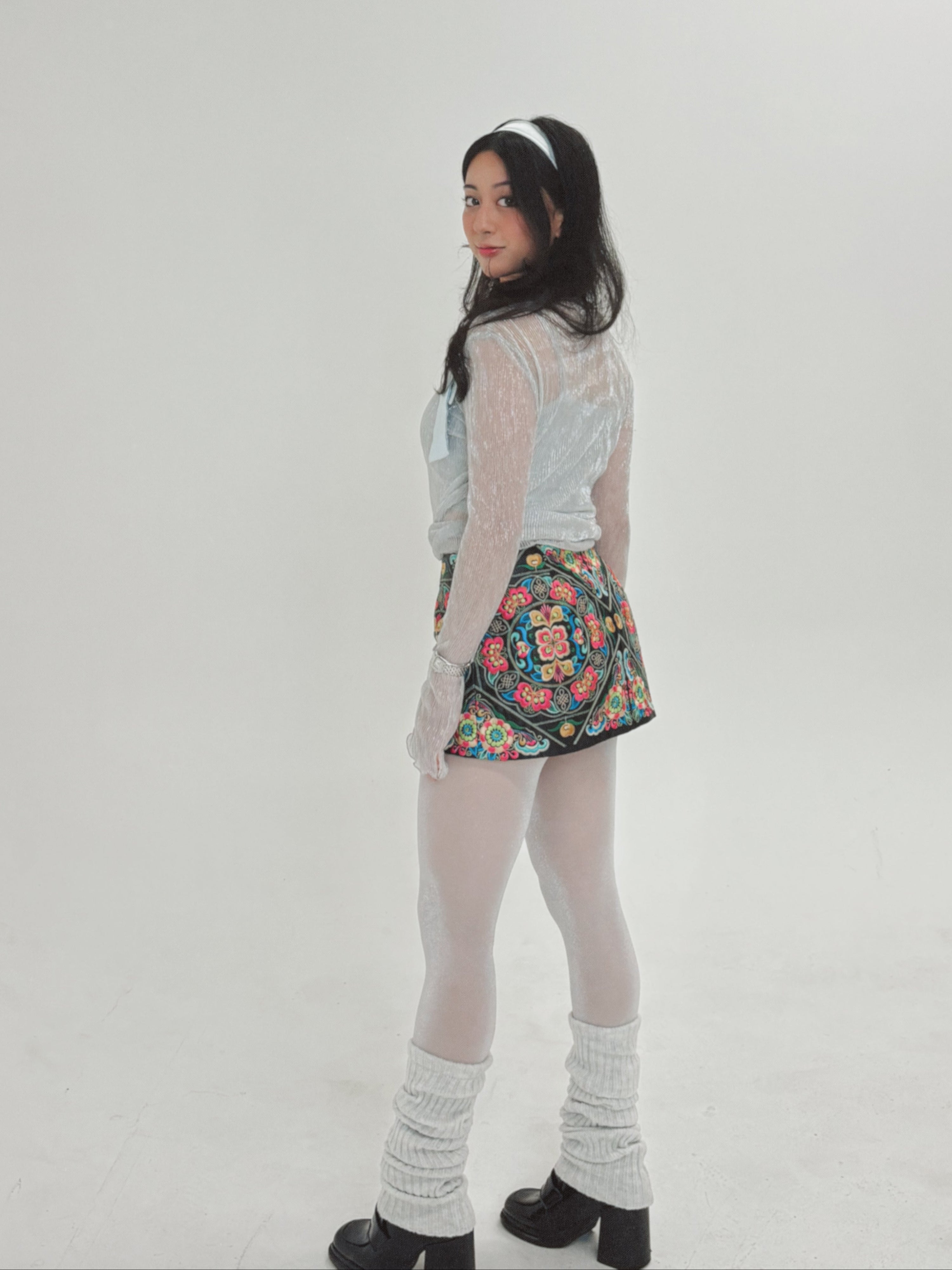Person wearing a floral skirt and white top on a plain background