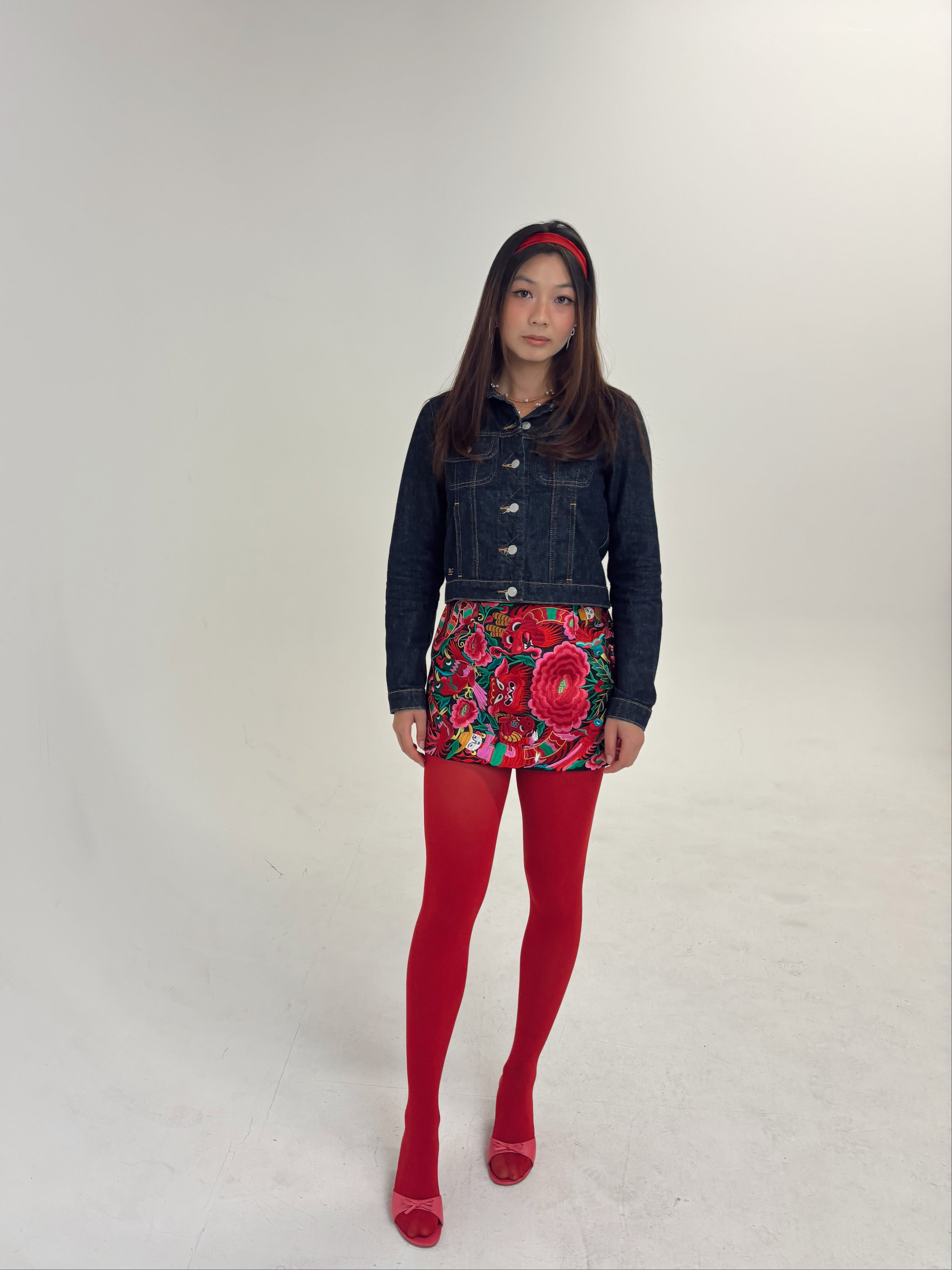 Person wearing a denim jacket, floral skirt, and red tights on a white background