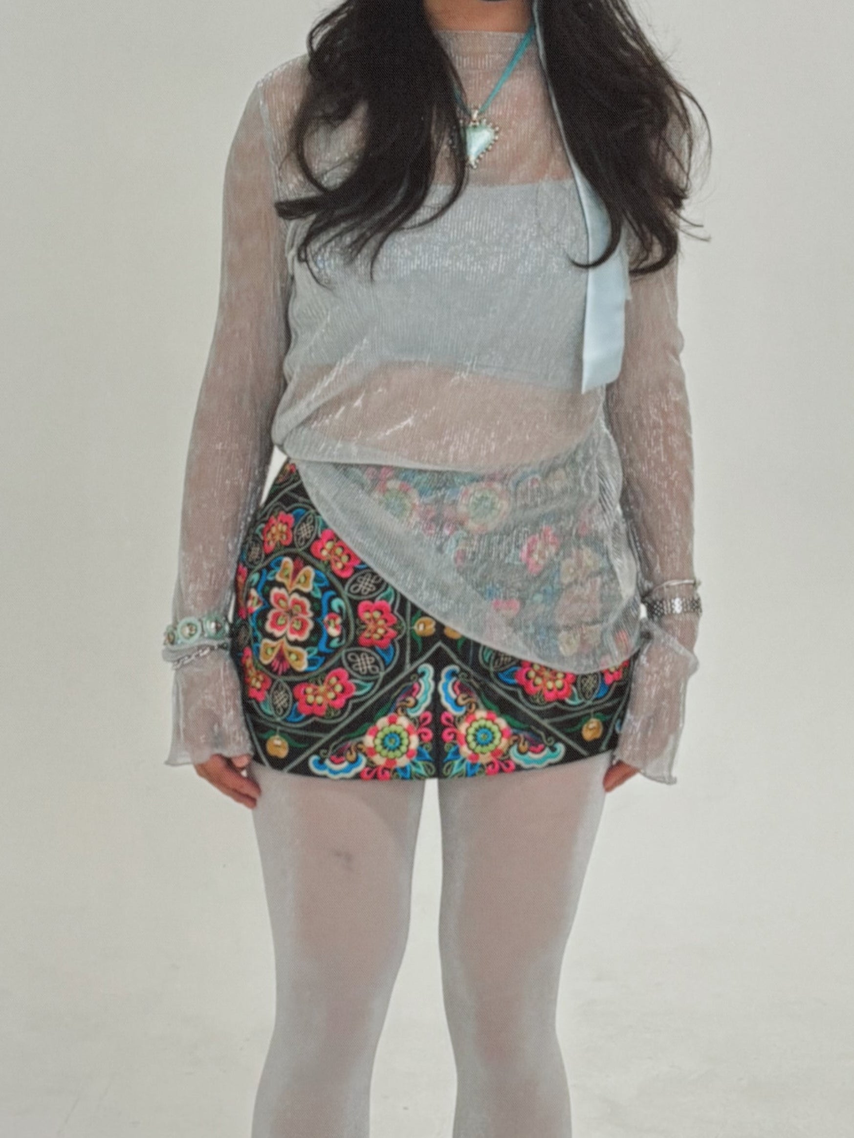 Person wearing a gray top, floral skirt, and patterned leggings on a plain background